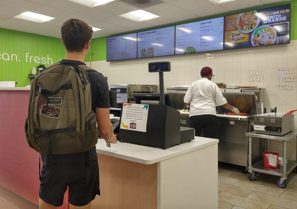 A Lipscomb student waiting in line at Freshens, with a warning sign about student IDs sitting in front of him